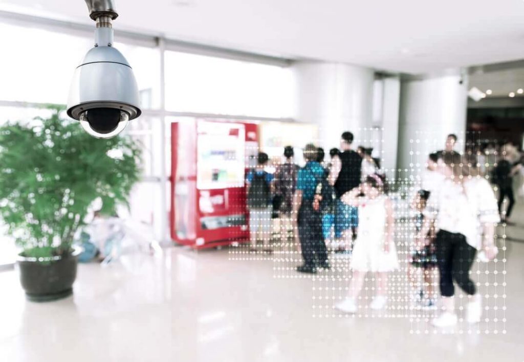 A surveillance camera hanging in a busy airport terminal.