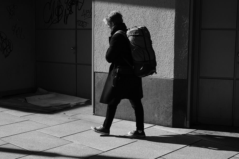 A young woman with a large backpack walking on the sidewalk during the daytime.